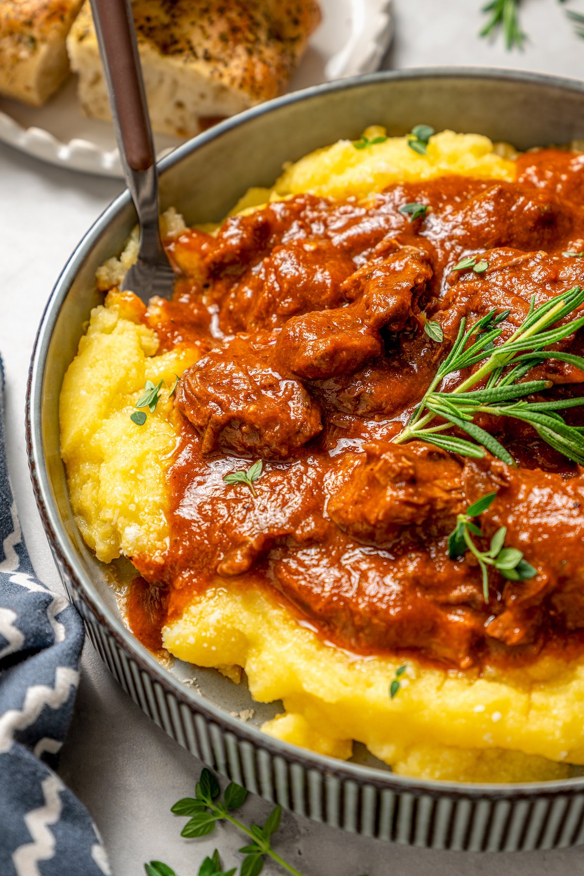 Angled photo of slow cooker short ribs with creamy polenta in a bowl, garnished with fresh rosemary. 